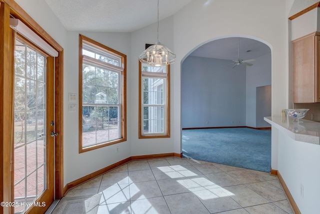 unfurnished dining area featuring ceiling fan with notable chandelier, a textured ceiling, arched walkways, light tile patterned flooring, and light colored carpet