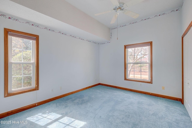 carpeted spare room featuring a wealth of natural light, ceiling fan, and baseboards