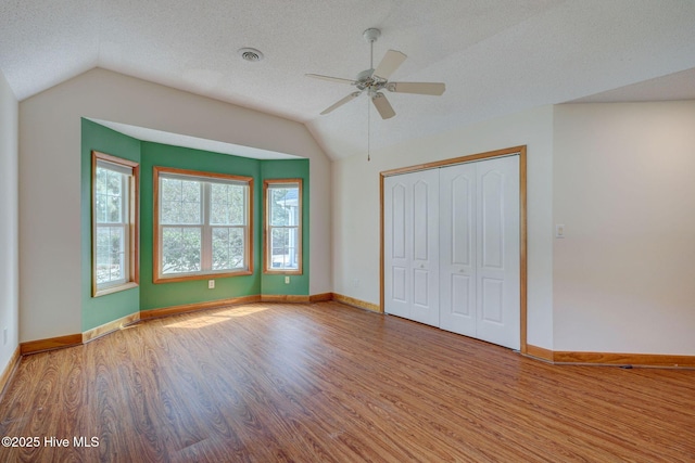 unfurnished bedroom with visible vents, baseboards, vaulted ceiling, wood finished floors, and a textured ceiling