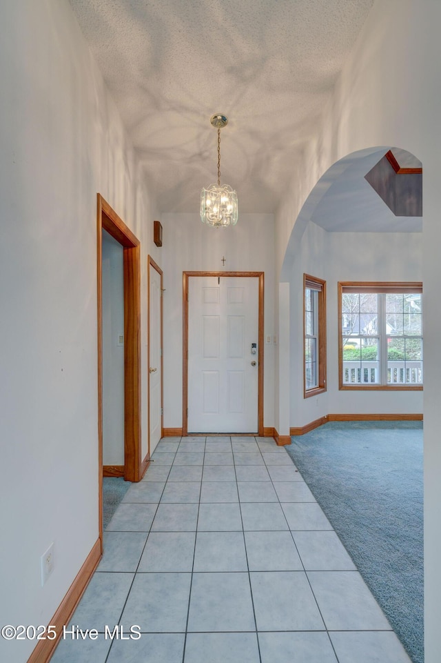 entrance foyer with arched walkways, light colored carpet, a textured ceiling, and baseboards