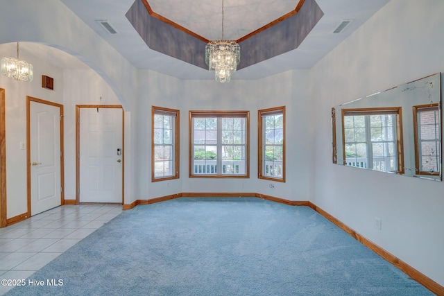 carpeted entrance foyer with visible vents, a raised ceiling, and an inviting chandelier