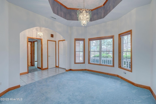 tiled spare room with a wealth of natural light, a raised ceiling, an inviting chandelier, and carpet floors