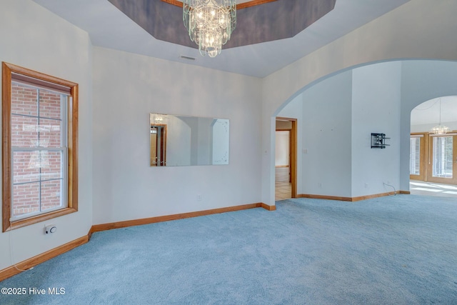 unfurnished room with baseboards, carpet floors, an inviting chandelier, arched walkways, and a raised ceiling