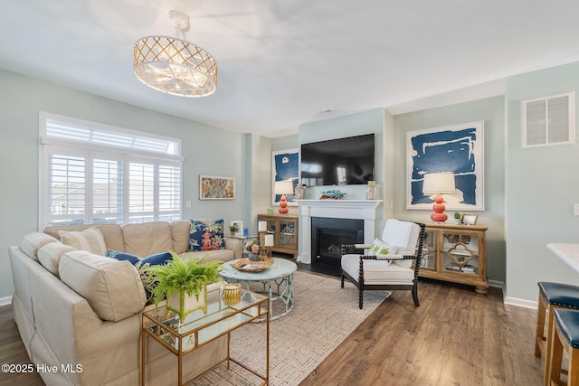 living area featuring visible vents, baseboards, a fireplace with flush hearth, and wood finished floors