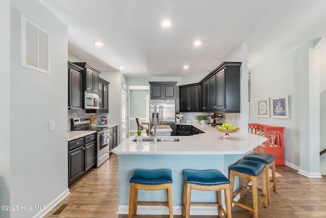 kitchen with a kitchen bar, light wood-style flooring, a sink, appliances with stainless steel finishes, and light countertops