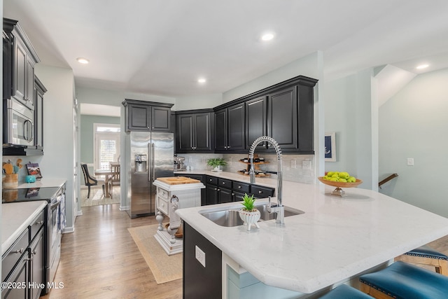 kitchen featuring light wood-type flooring, a breakfast bar, a sink, appliances with stainless steel finishes, and decorative backsplash