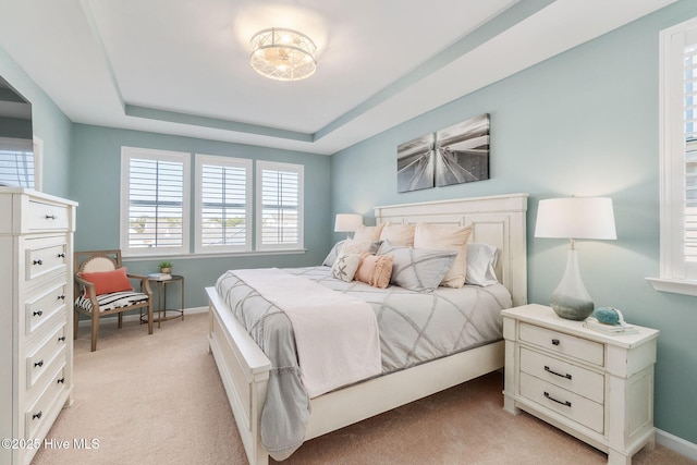 bedroom featuring baseboards, a raised ceiling, and light colored carpet