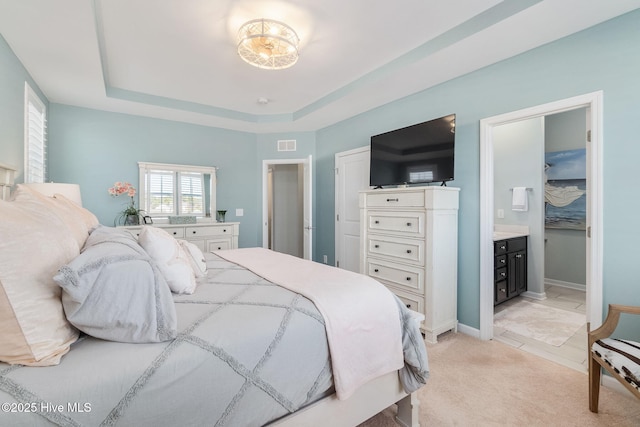 bedroom with visible vents, ensuite bathroom, a tray ceiling, baseboards, and light colored carpet