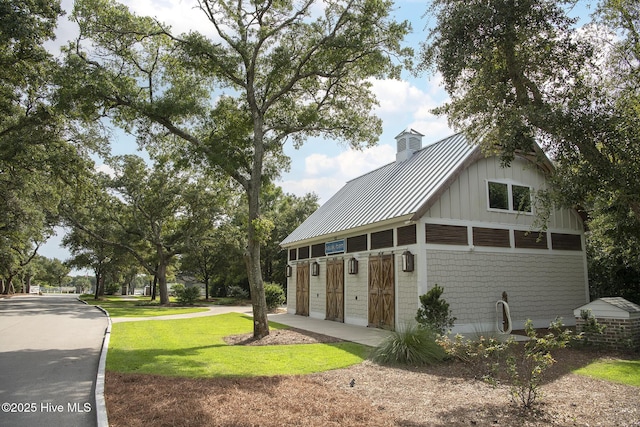 view of front facade with brick siding, board and batten siding, a front yard, metal roof, and a garage