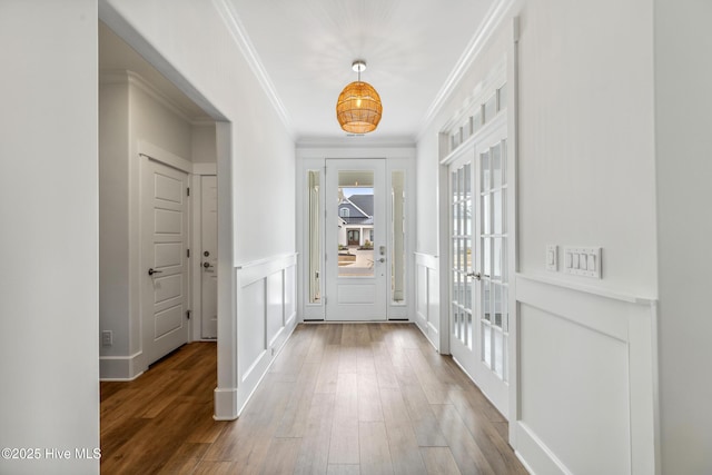 foyer entrance with wainscoting, wood finished floors, ornamental molding, and a decorative wall