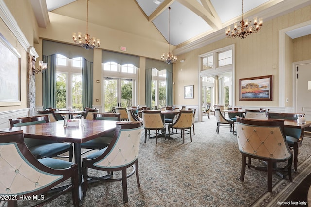 carpeted dining room featuring a decorative wall, high vaulted ceiling, and an inviting chandelier