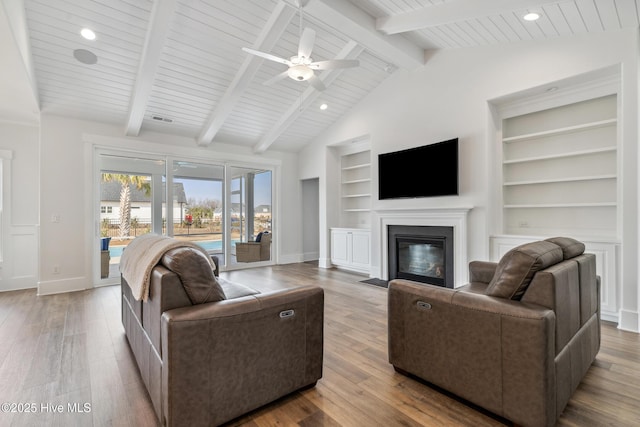 living room featuring baseboards, lofted ceiling with beams, a ceiling fan, wood finished floors, and a fireplace with flush hearth