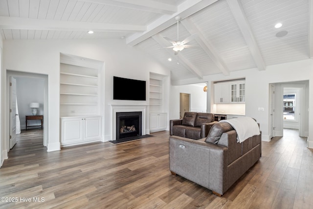 living room featuring baseboards, a ceiling fan, a fireplace with flush hearth, vaulted ceiling with beams, and wood finished floors