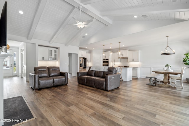 living area featuring wood finished floors, ceiling fan with notable chandelier, beam ceiling, and recessed lighting