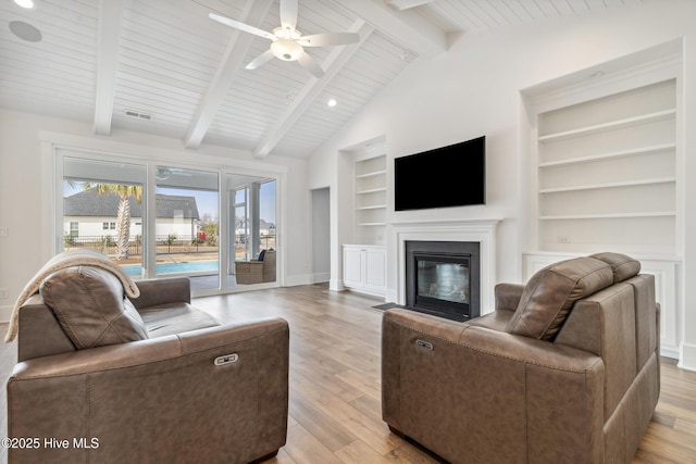 living area with a glass covered fireplace, built in features, visible vents, light wood finished floors, and vaulted ceiling with beams
