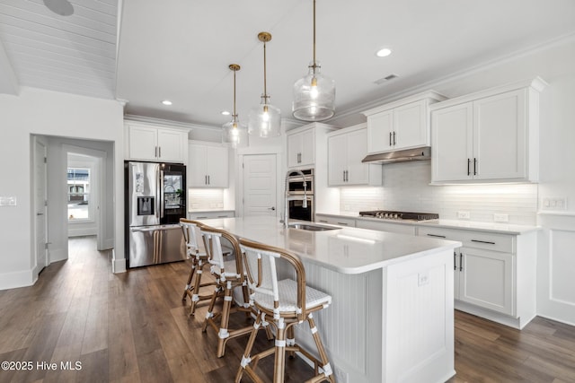 kitchen with visible vents, an island with sink, under cabinet range hood, stainless steel appliances, and backsplash