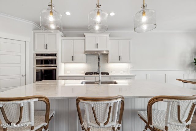 kitchen featuring double oven, backsplash, crown molding, pendant lighting, and a kitchen island with sink