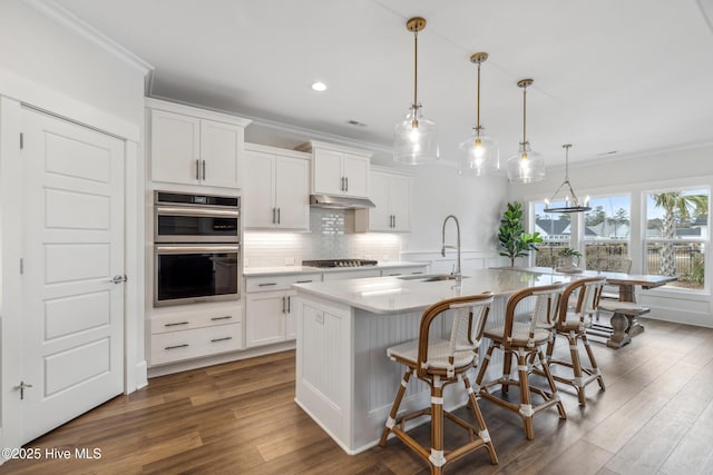 kitchen with stainless steel double oven, a sink, dark wood-type flooring, and ornamental molding