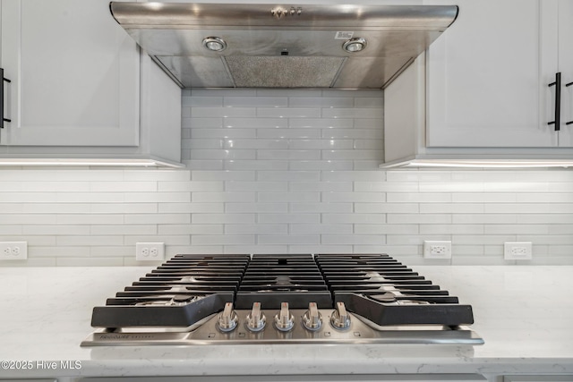 room details with stainless steel gas cooktop, extractor fan, backsplash, and white cabinets