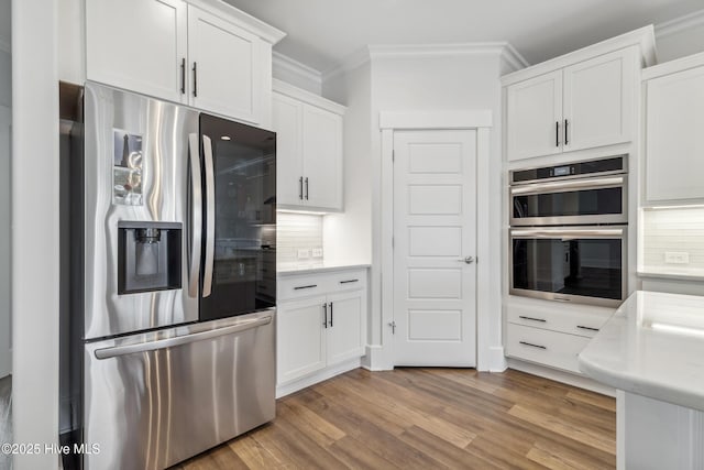 kitchen with ornamental molding, light countertops, appliances with stainless steel finishes, white cabinetry, and decorative backsplash