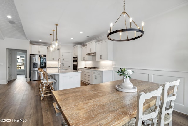 dining space featuring crown molding, dark wood-type flooring, a wainscoted wall, a chandelier, and recessed lighting
