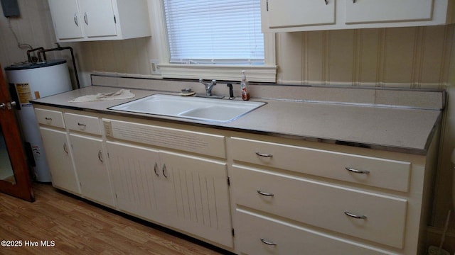 kitchen with light wood finished floors, white cabinets, water heater, and a sink