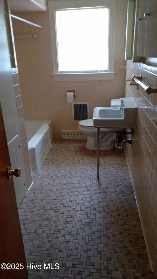 full bath featuring tile walls, visible vents, toilet, and a baseboard heating unit