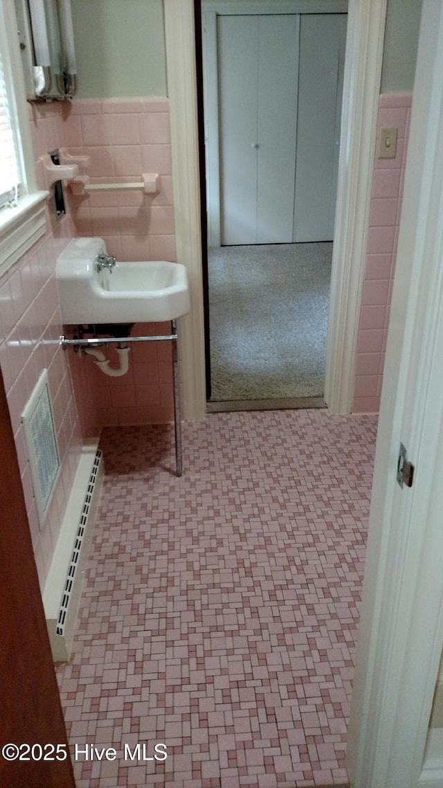 bathroom featuring visible vents, a baseboard radiator, a sink, wainscoting, and tile walls