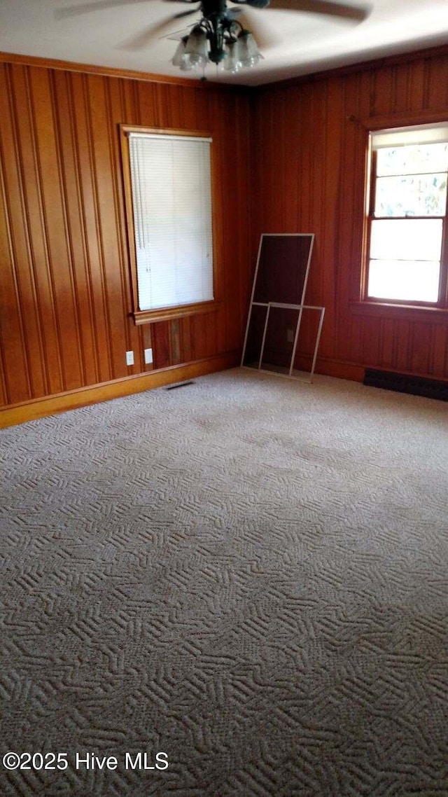 unfurnished room with visible vents, carpet floors, ceiling fan, and wood walls