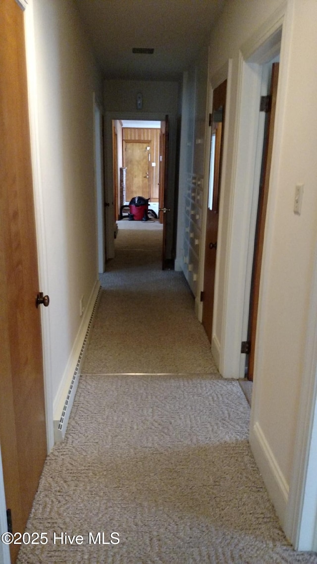 hall featuring a baseboard heating unit, baseboards, visible vents, and carpet flooring