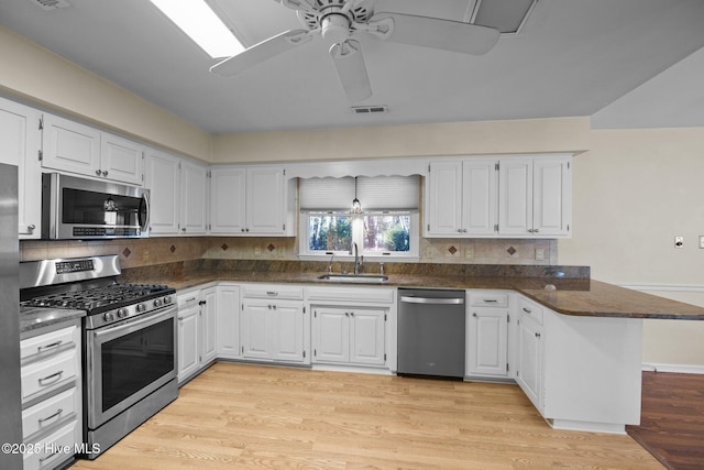 kitchen with ceiling fan, appliances with stainless steel finishes, a peninsula, light wood-style floors, and a sink