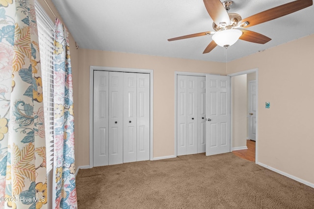 unfurnished bedroom with two closets, baseboards, carpet, and a ceiling fan