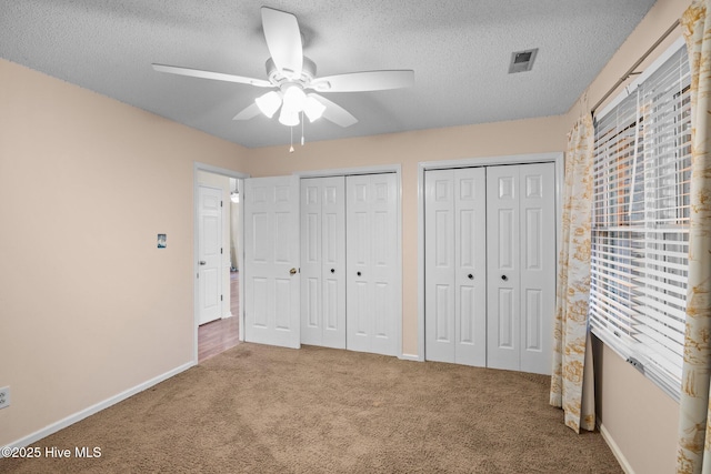 unfurnished bedroom with baseboards, multiple closets, carpet flooring, a textured ceiling, and a ceiling fan