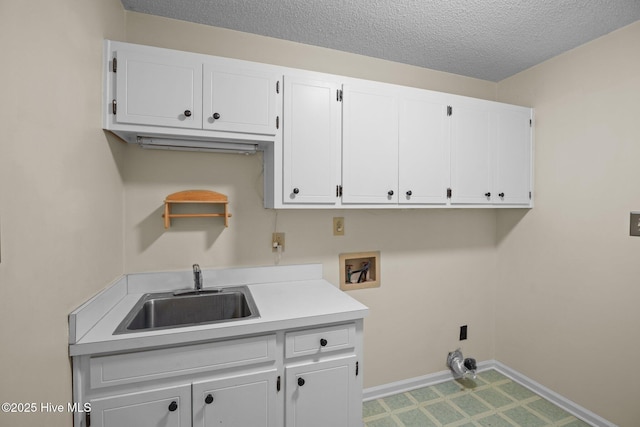 laundry area featuring hookup for a washing machine, baseboards, cabinet space, a sink, and a textured ceiling