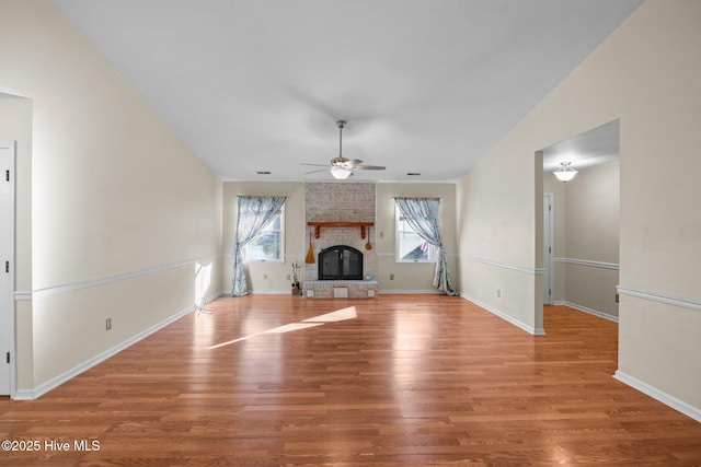 unfurnished living room featuring baseboards, vaulted ceiling, a fireplace, wood finished floors, and a ceiling fan