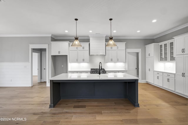 kitchen with white cabinetry, custom exhaust hood, light wood-style floors, and a kitchen island with sink