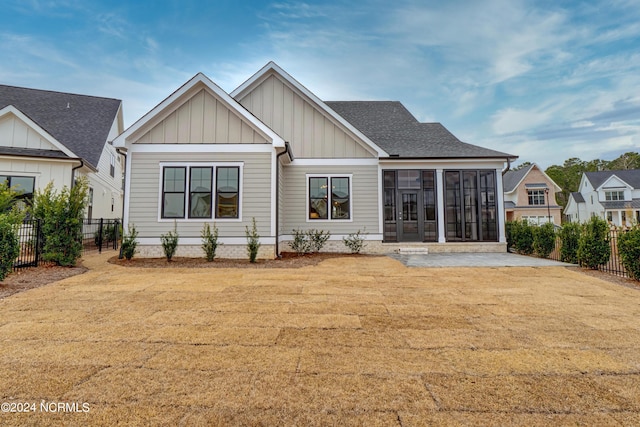 rear view of house with board and batten siding, fence, a yard, and a sunroom