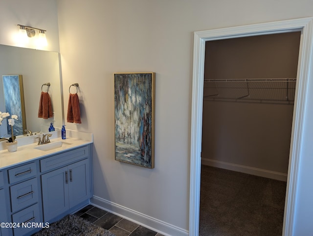 bathroom with vanity, a walk in closet, and baseboards