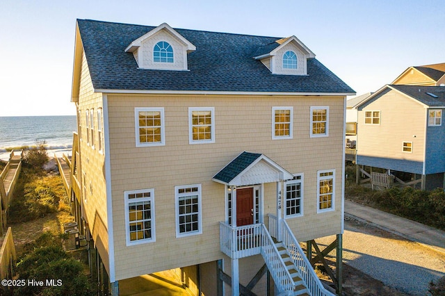 coastal inspired home with stairway, roof with shingles, and a water view