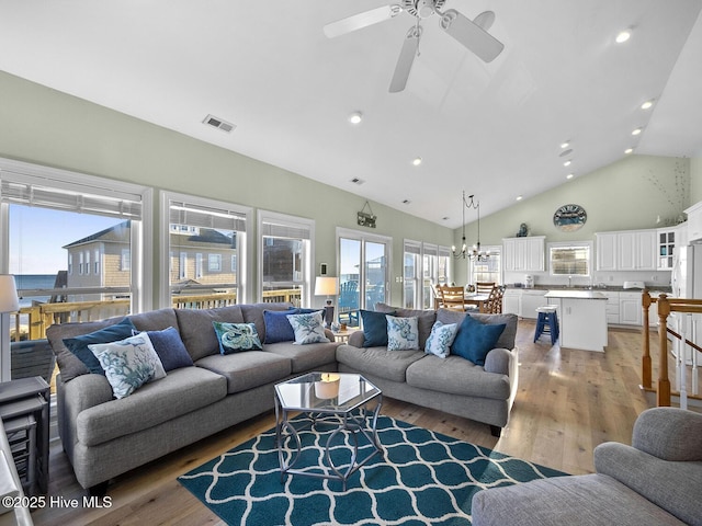 living room with light wood finished floors, visible vents, ceiling fan with notable chandelier, recessed lighting, and high vaulted ceiling