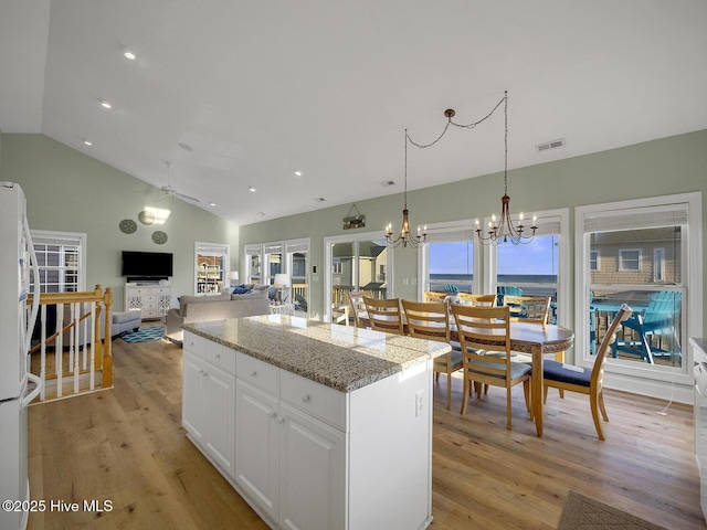 kitchen featuring visible vents, light wood finished floors, a kitchen island, vaulted ceiling, and white cabinets