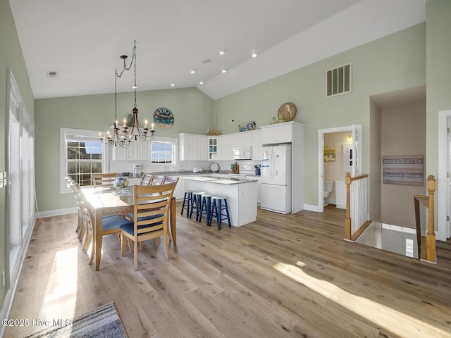 dining room featuring light wood-style flooring, visible vents, and high vaulted ceiling