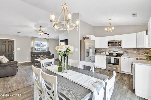 dining space featuring wood finished floors, baseboards, visible vents, vaulted ceiling, and ceiling fan with notable chandelier