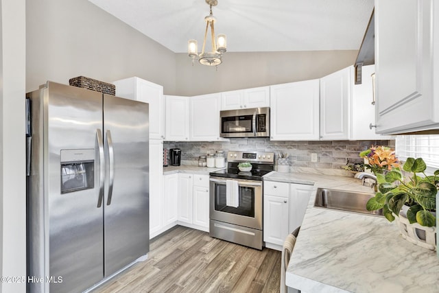 kitchen with a sink, appliances with stainless steel finishes, white cabinets, decorative backsplash, and vaulted ceiling