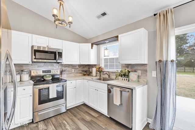 kitchen with visible vents, a sink, backsplash, stainless steel appliances, and vaulted ceiling