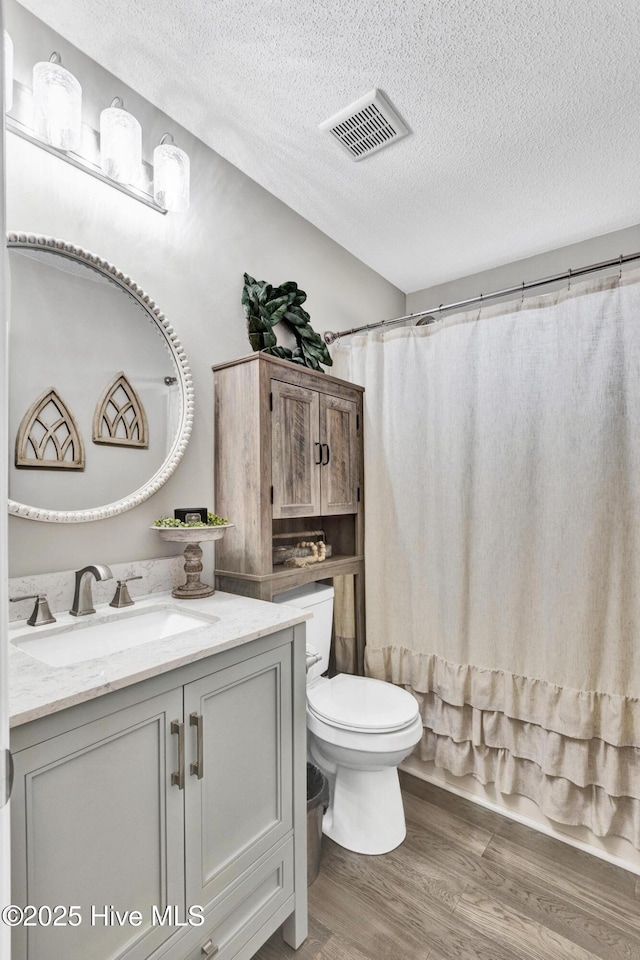 bathroom featuring vanity, wood finished floors, visible vents, a textured ceiling, and toilet