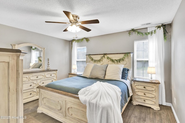 bedroom with visible vents, a textured ceiling, baseboards, ceiling fan, and dark wood-style flooring