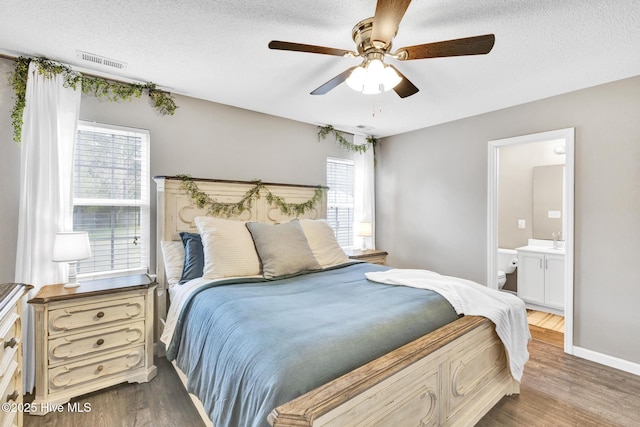 bedroom featuring visible vents, a textured ceiling, ensuite bathroom, and wood finished floors