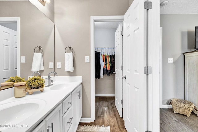 full bathroom with a textured ceiling, double vanity, wood finished floors, and a sink