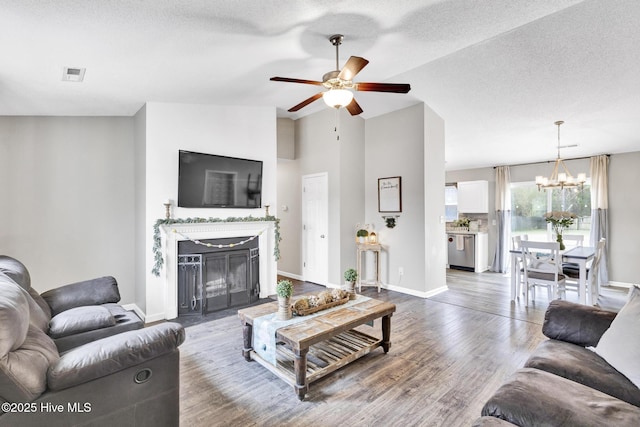 living room with wood finished floors, visible vents, a fireplace, vaulted ceiling, and ceiling fan with notable chandelier